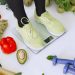 Person standing on scales surrounded by fresh produce and fitness equipment symbolizing a balanced lifestyle.