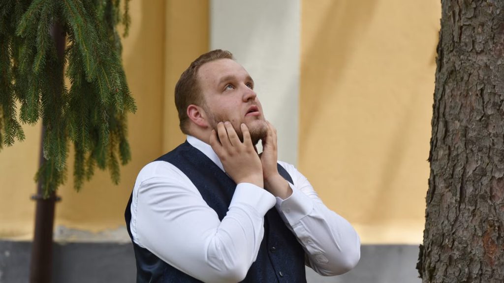 A man in formal attire looks contemplative under trees in Vásárosnamény.